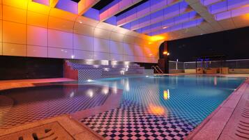 Une piscine intérieure avec des carreaux de sol à motifs géométriques, un mur recouvert de carreaux formant un motif géométrique, et un plafond doté de panneaux lumineux.