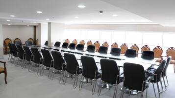 A conference room with a long table and rows of chairs, large windows, and a white ceiling.