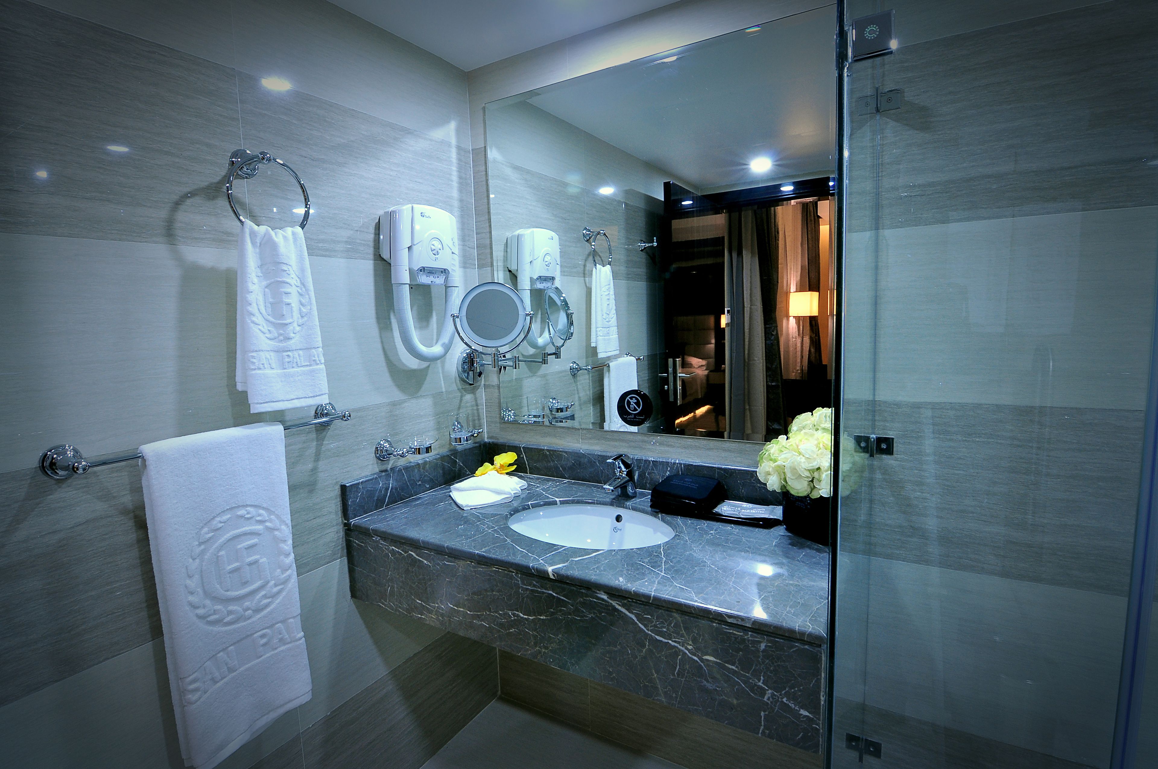 Une salle de bain moderne avec un lavabo en marbre, deux urinoirs, un porte-serviettes et un grand miroir.