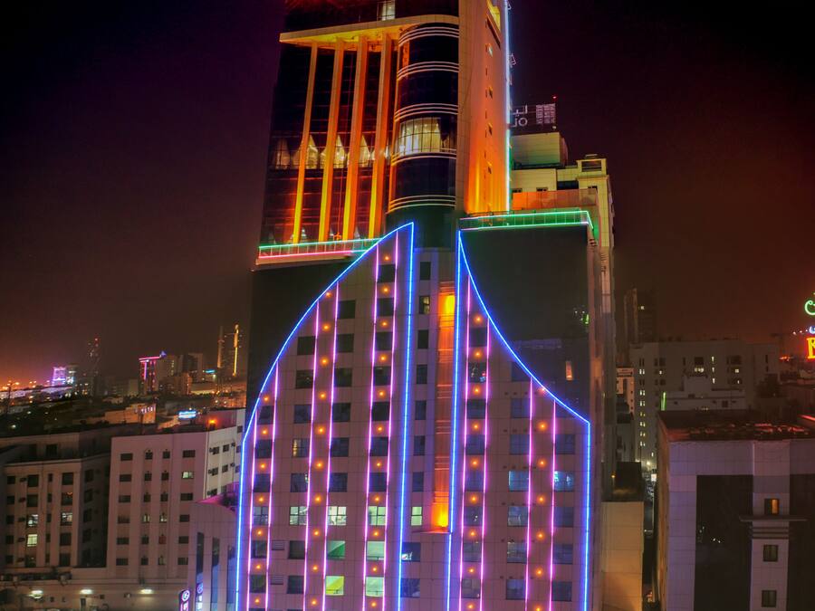 Un edificio alto con líneas verticales iluminadas y una entrada destacada en la base.