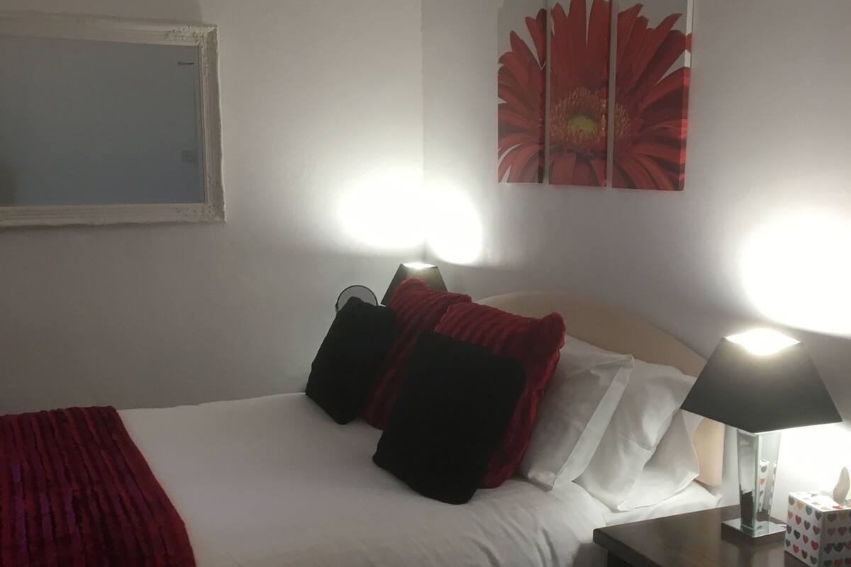 Ett hotellrum med en säng, två sänglampor, ett nattduksbord med en näsdukslåda och ett stort blommotiv på väggen.