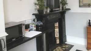 A modern kitchen with a black countertop, a microwave, a coffee maker, and a black stove. There are two potted plants on the stove and a flat-screen TV above it. - Garswood Guesthouse (Penzance)