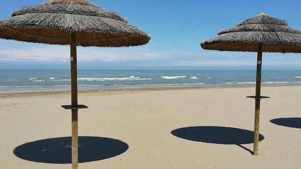 Zwei strohgedeckte Sonnenschirme an einem sandigen Strand mit dem Meer im Hintergrund.