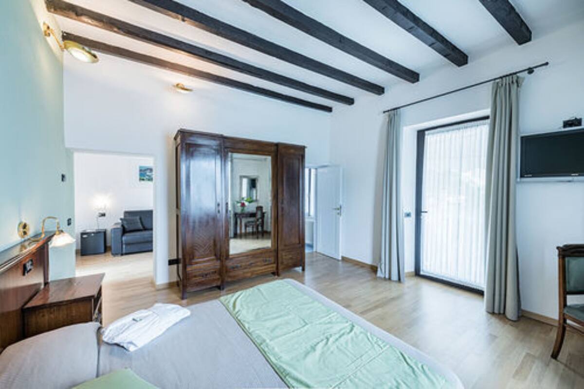Une pièce spacieuse avec un grand lit, une armoire en bois et une porte-fenêtre coulissante donnant sur un balcon.