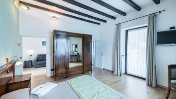 A spacious room with a large bed, wooden wardrobe, and a sliding glass door leading to a balcony.