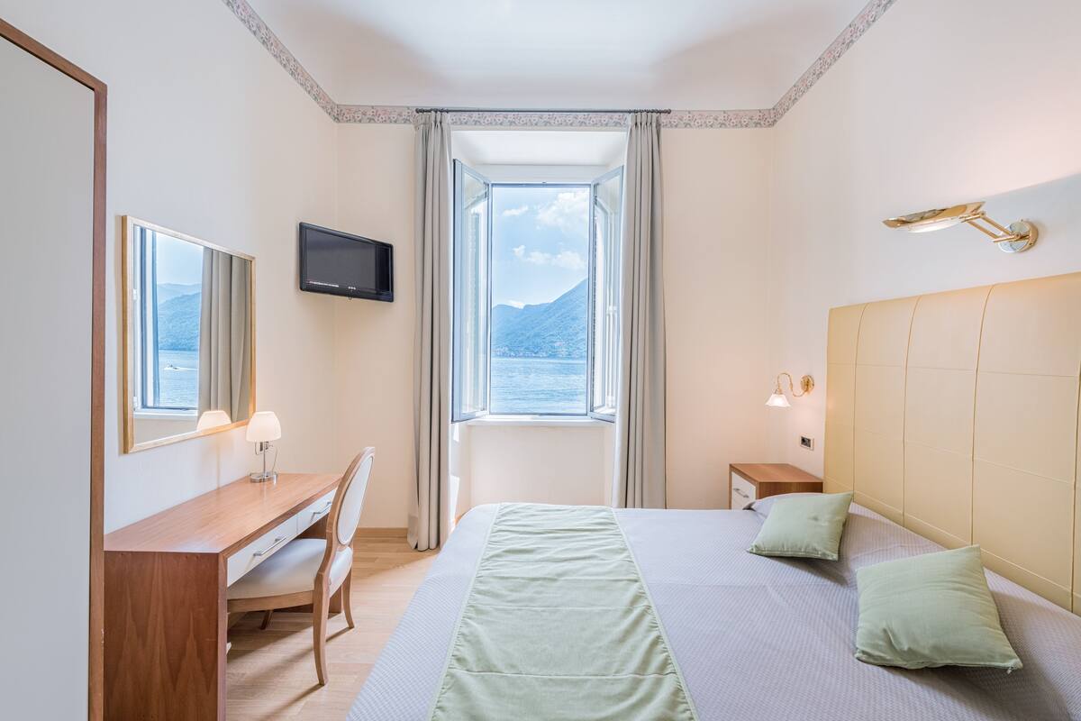 Une chambre d’hôtel comprenant un lit, un bureau, une chaise, une télévision, une fenêtre donnant sur la montagne et une lampe de chevet.