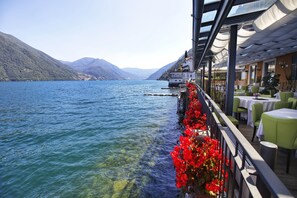 A lakeside restaurant with outdoor seating overlooking a calm lake and mountains.