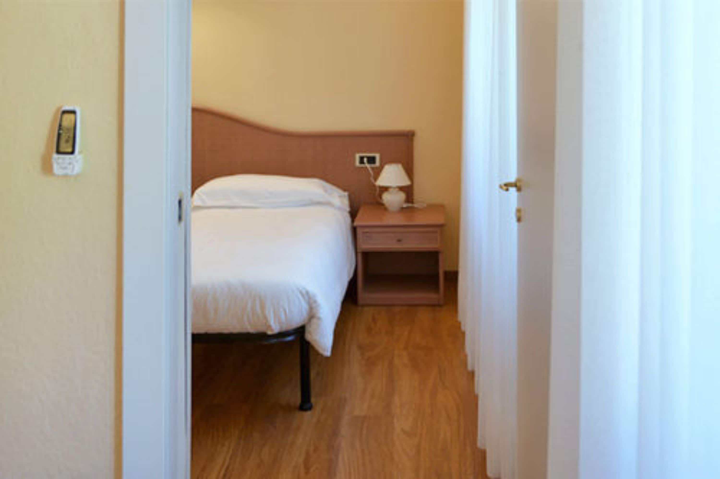 Una habitación de hotel con cama, mesita de noche, lámpara y teléfono en la pared.