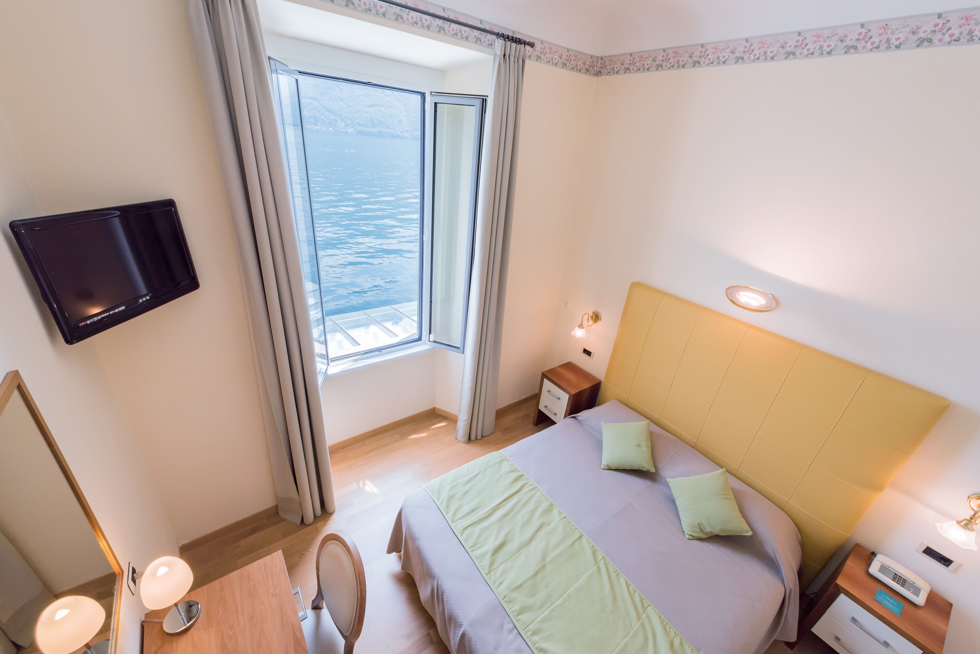 Une chambre d’hôtel équipée d’un lit, d’une table de chevet, d’une commode, d’une lampe et d’un téléviseur fixé au mur.