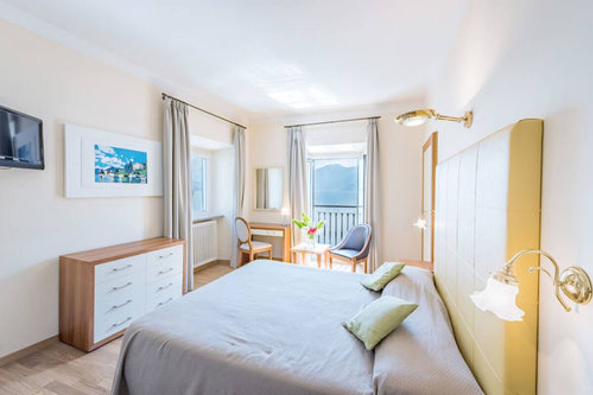 Une chambre d’hôtel avec un lit, un bureau, une chaise, une télévision et une fenêtre avec des rideaux.