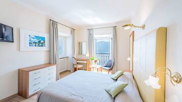 Habitación de hotel con cama, escritorio, silla, televisión y ventana con cortinas.
