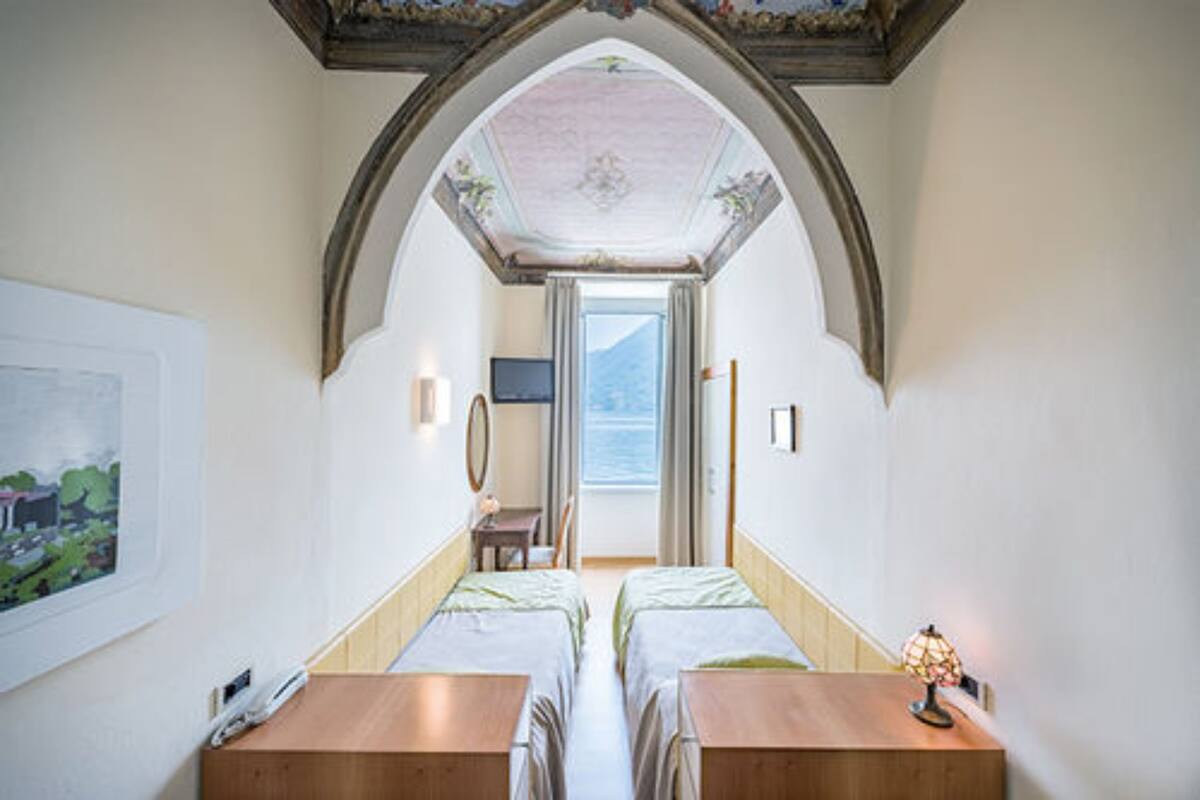 Une chambre avec deux lits, une table en bois, une lampe et une vue sur la mer par la porte.