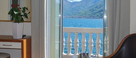 A balcony with a view of a lake and mountains, a wooden table with a chair, and a potted plant.