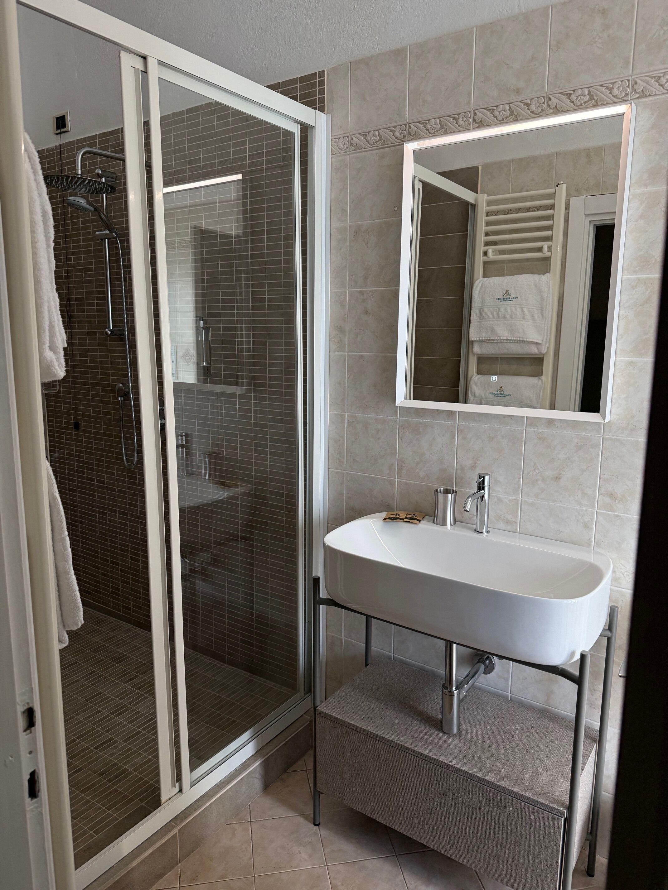 Un baño moderno con ducha de vidrio, un lavamanos blanco y un espejo encima.