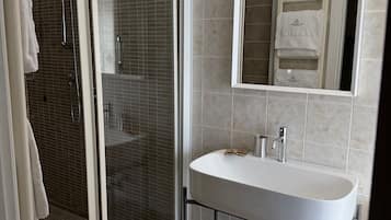 Un baño moderno con ducha de vidrio, un lavamanos blanco y un espejo encima.