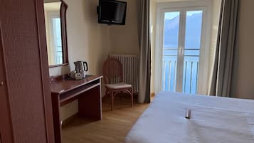 A hotel room with a bed, a desk with a kettle, a chair, a television, and a view of the sea.