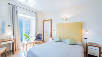 Habitación de hotel con una cama grande, un escritorio, una silla, una mesita de noche y un ventanal con cortinas.