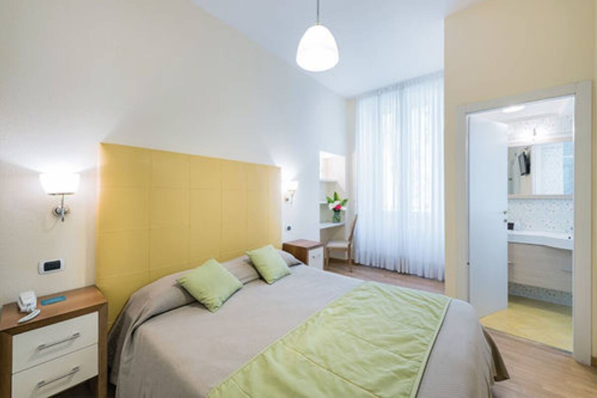 Une chambre d’hôtel comprenant un lit, une table de chevet, une lampe et un dressing.