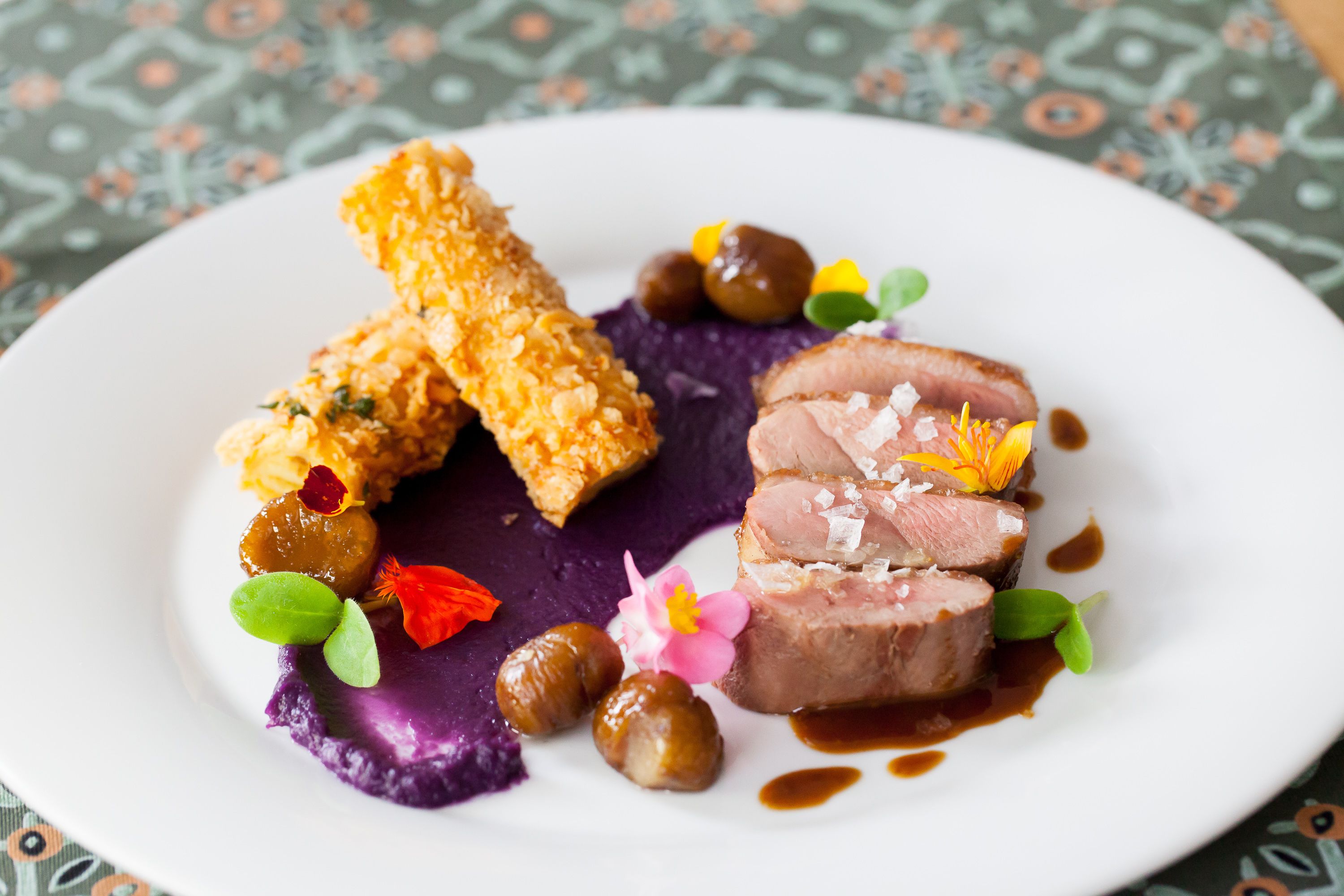 Un plato de comida con diversos ingredientes, incluyendo un trozo de carne, algo empanizado y algunas guarniciones.