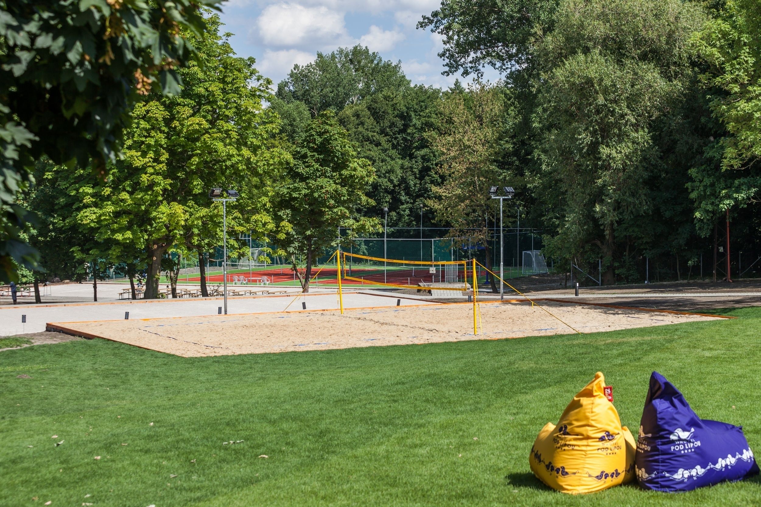 A volleyball court surrounded by trees, with two bean bags on the grass.