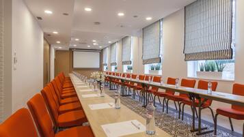 Un salón de conferencias con una larga mesa, sillas color naranja y una pantalla de proyector.