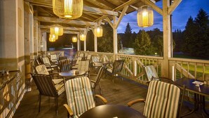 An outdoor patio with wicker hanging lamps, striped cushioned chairs, and tables. - Hotel Pod Lipou (Modra)