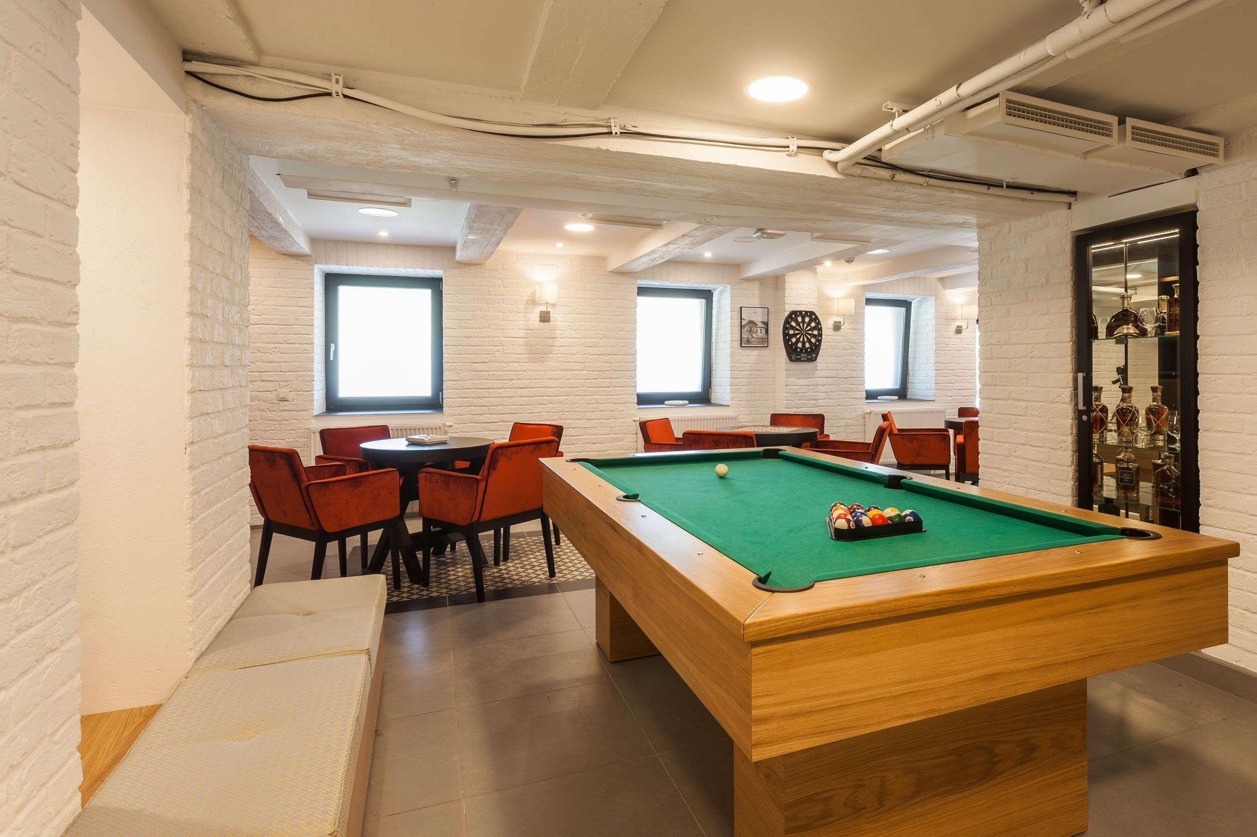 Ein Billardraum mit Pooltisch, roten Sesseln und einem kleinen Essbereich mit Tisch und Stühlen.