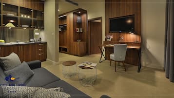 Une chambre d’hôtel moderne équipée d’un canapé, d’une table basse et d’un bureau avec une chaise. On y trouve également un coin cuisine avec des placards et un téléviseur fixé au mur.