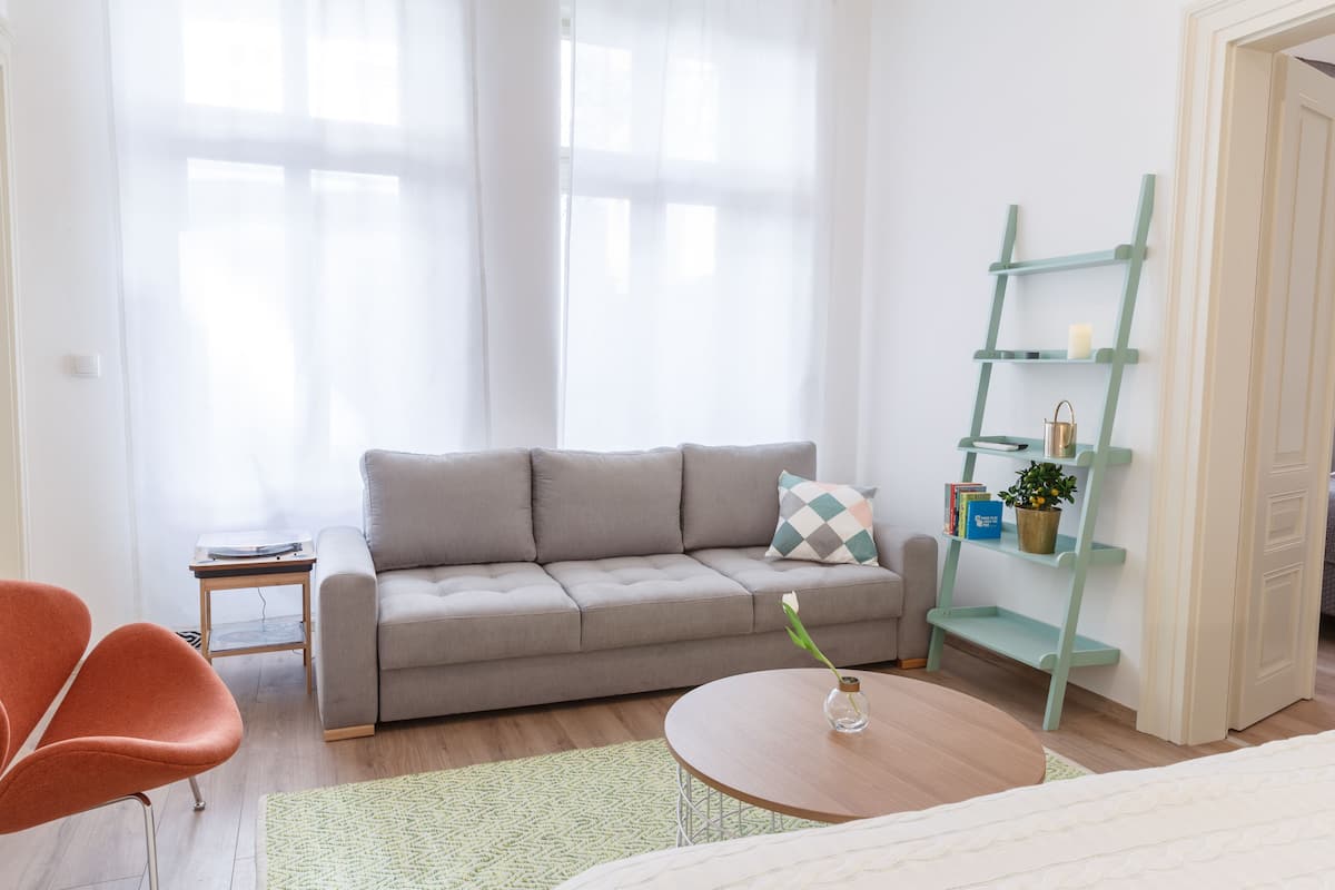 A living room with a grey sofa, a small side table, a round coffee table with a vase, and a green ladder shelf against the wall.
