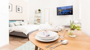 A neatly arranged hotel room with a bed, bedside table with a vase of flowers, a dining table set with plates, glasses, and cutlery. - CHILL Apartments (Prague)
