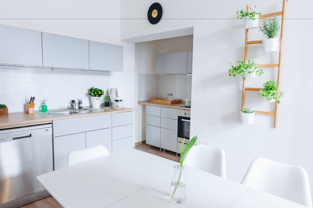 A modern kitchen with white cabinets, a dishwasher, and a dining area with a white table and chairs.