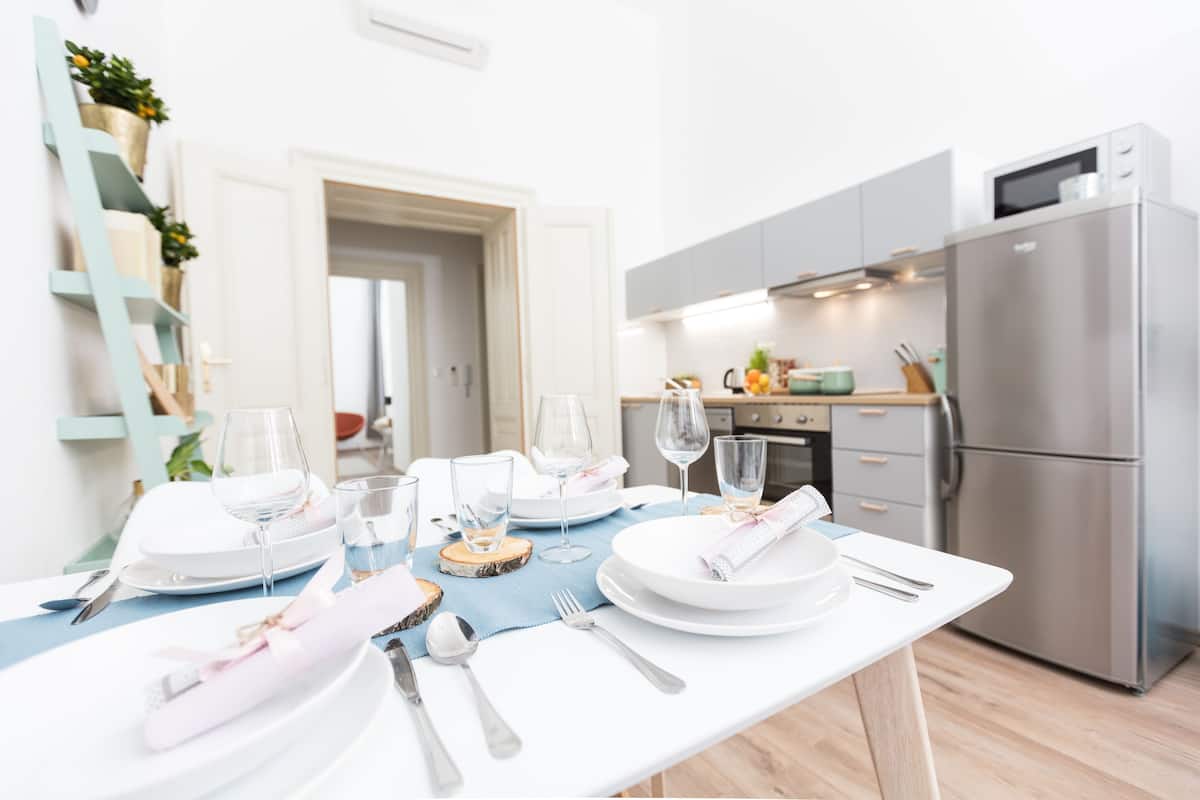 A modern kitchen with stainless steel appliances, a dining table set with white plates, glasses, and cutlery.