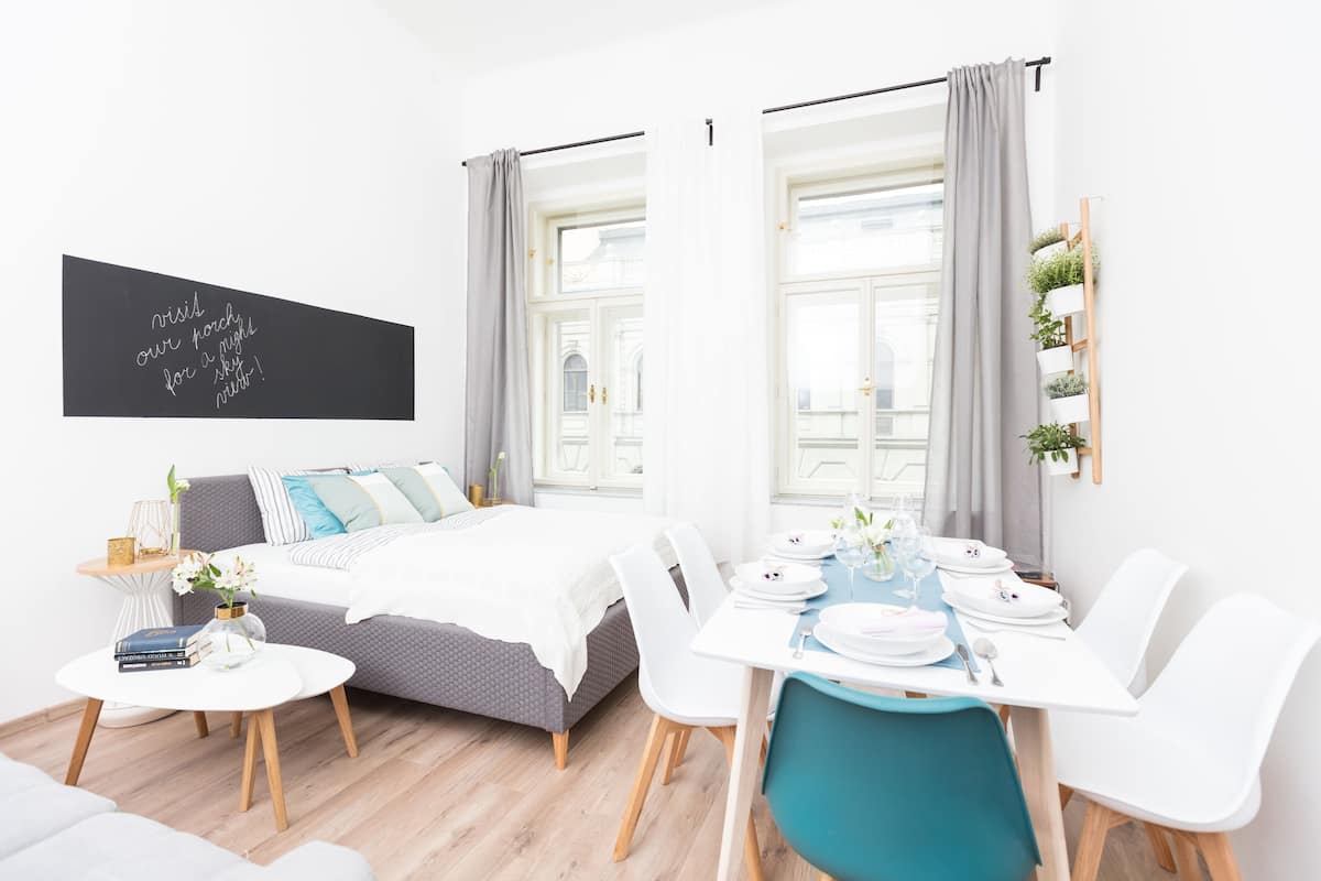 A modern hotel room with a bed, a dining table set for two, and a small seating area.