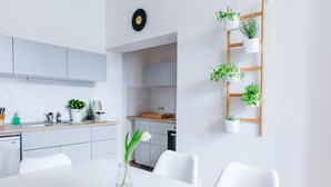 A modern kitchen with white cabinets, a wooden countertop, and a dining area with a white table and chairs. There are potted plants on a wooden ladder, and a vase with a single white flower on the dining table. - CHILL Apartments (Prague)