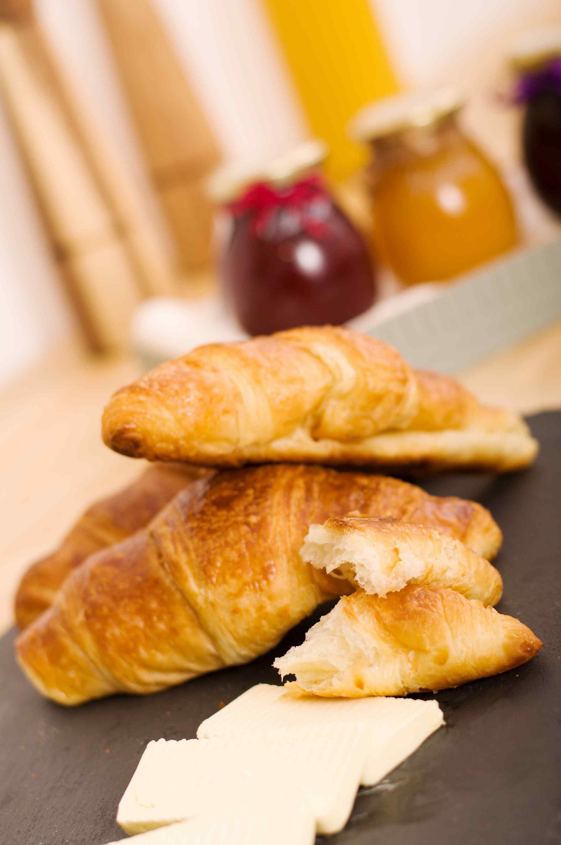 En hög med croissanter på en mörk yta, med en kniv och ett marmeladglas i bakgrunden.