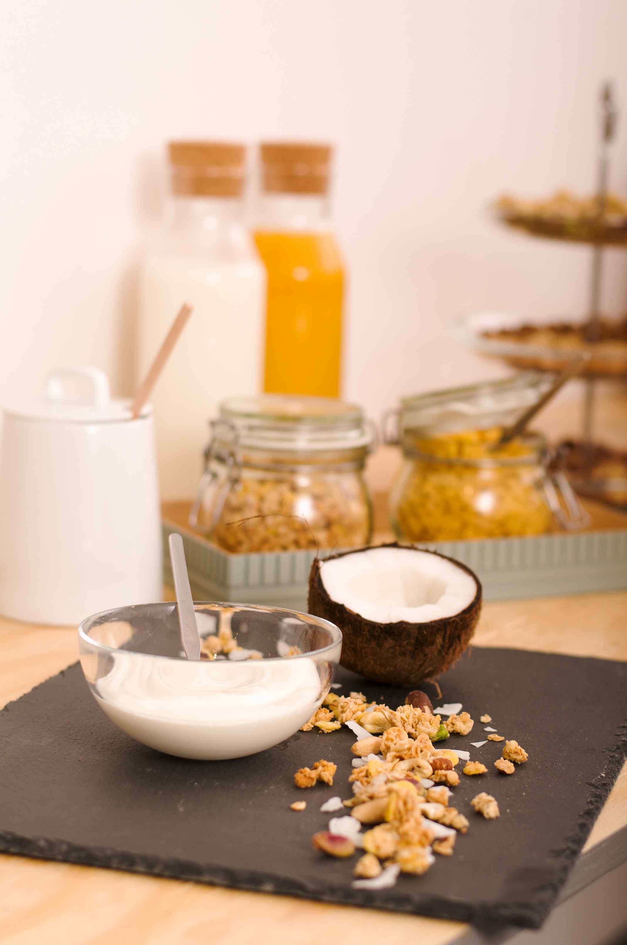 Presentación de desayuno con un tazón de yogur, granola y media coco sobre un plato de pizarra negra.