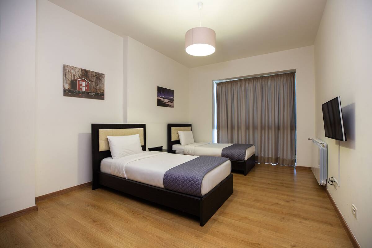 Une chambre d’hôtel avec deux lits, un téléviseur à écran plat, une fenêtre avec des rideaux et des œuvres d’art accrochées aux murs.