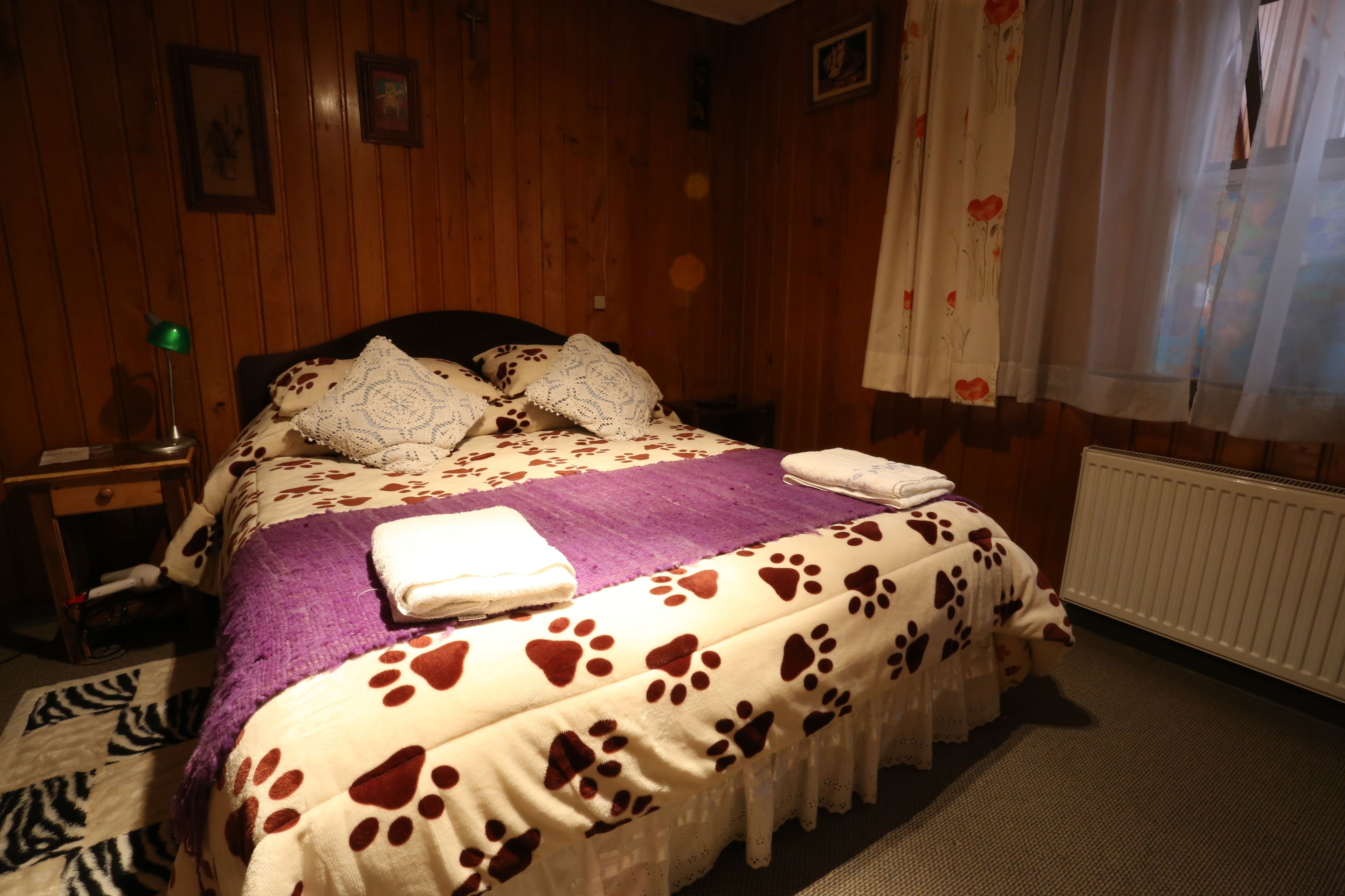 A bedroom with wooden walls, a bed with a patterned blanket, a purple throw, and a white radiator.