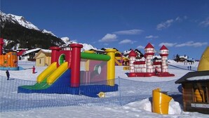 Schneebedecktes Areal im Freien mit aufblasbaren Spielgeräten und einem Berg im Hintergrund.