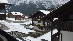 Ein verschneites Bergdorf mit Holzhäusern und einer Steintreppe, die zu einer Holzterrasse führt.