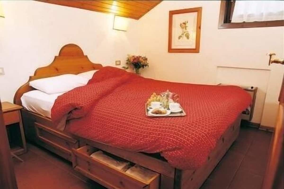 Una cama individual con estructura de madera, una colcha roja y una bandeja de comida sobre la cama.