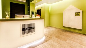 A reception desk with a laptop, a potted plant, and a decorative item on the counter. - M2M Made To Measure (Milan)