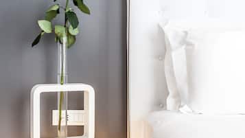 Um quarto moderno com uma cama branca, uma mesa de cabeceira com um vaso de uma rosa branca e um abajur branco.