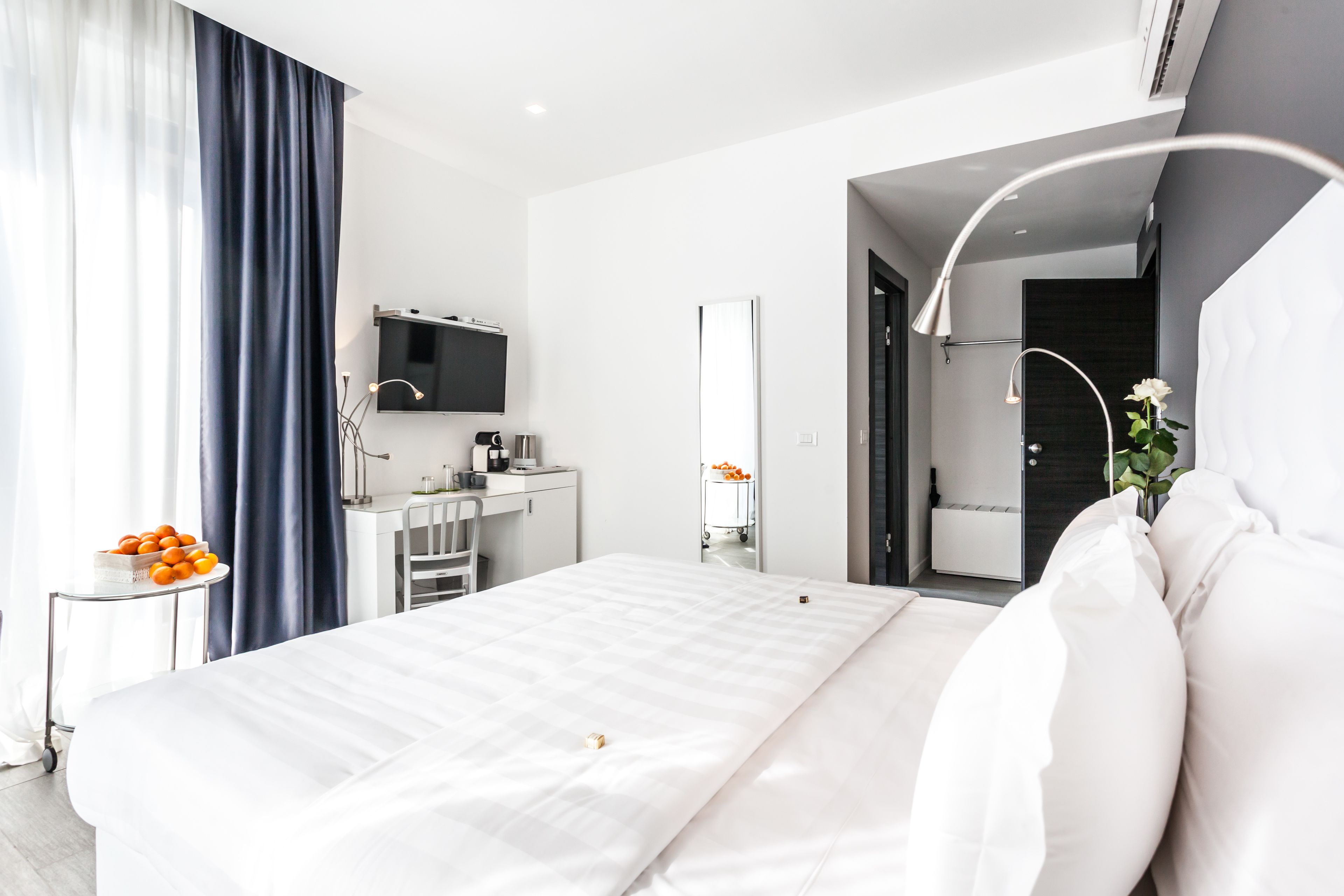 A modern hotel room with a large bed, a desk with a computer, a TV, and a bathroom visible through an open door.