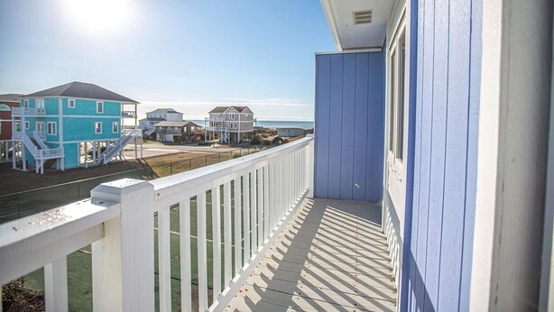 A balcony with a white railing overlooking a beach with houses in the background. - Feelin' Beachy-7a 2 Bedroom Home by RedAwning (Supply)