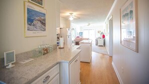A kitchen with granite countertops, white cabinets, and a central island. There are framed pictures on the walls and a ceiling fan. - Feelin' Beachy-7a 2 Bedroom Home by RedAwning (Supply)