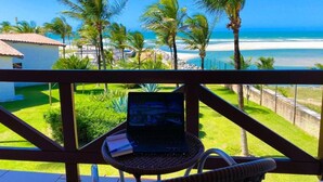 Een laptop op een rieten stoel met uitzicht op een strand, palmbomen en een heldere blauwe lucht.