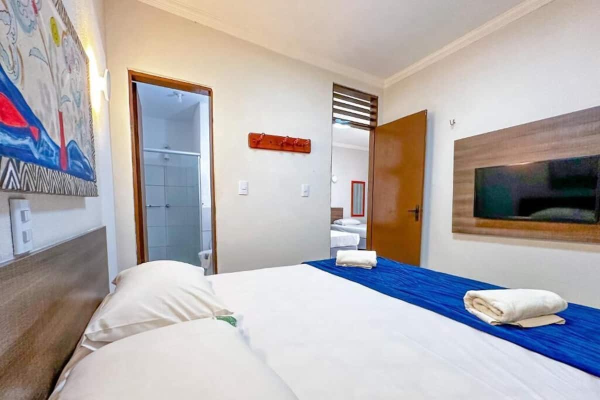 A hotel room with a large bed, a TV mounted on the wall, and a painting on the wall.