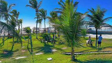 A grassy area with palm trees, a swing set, and a beach in the background.