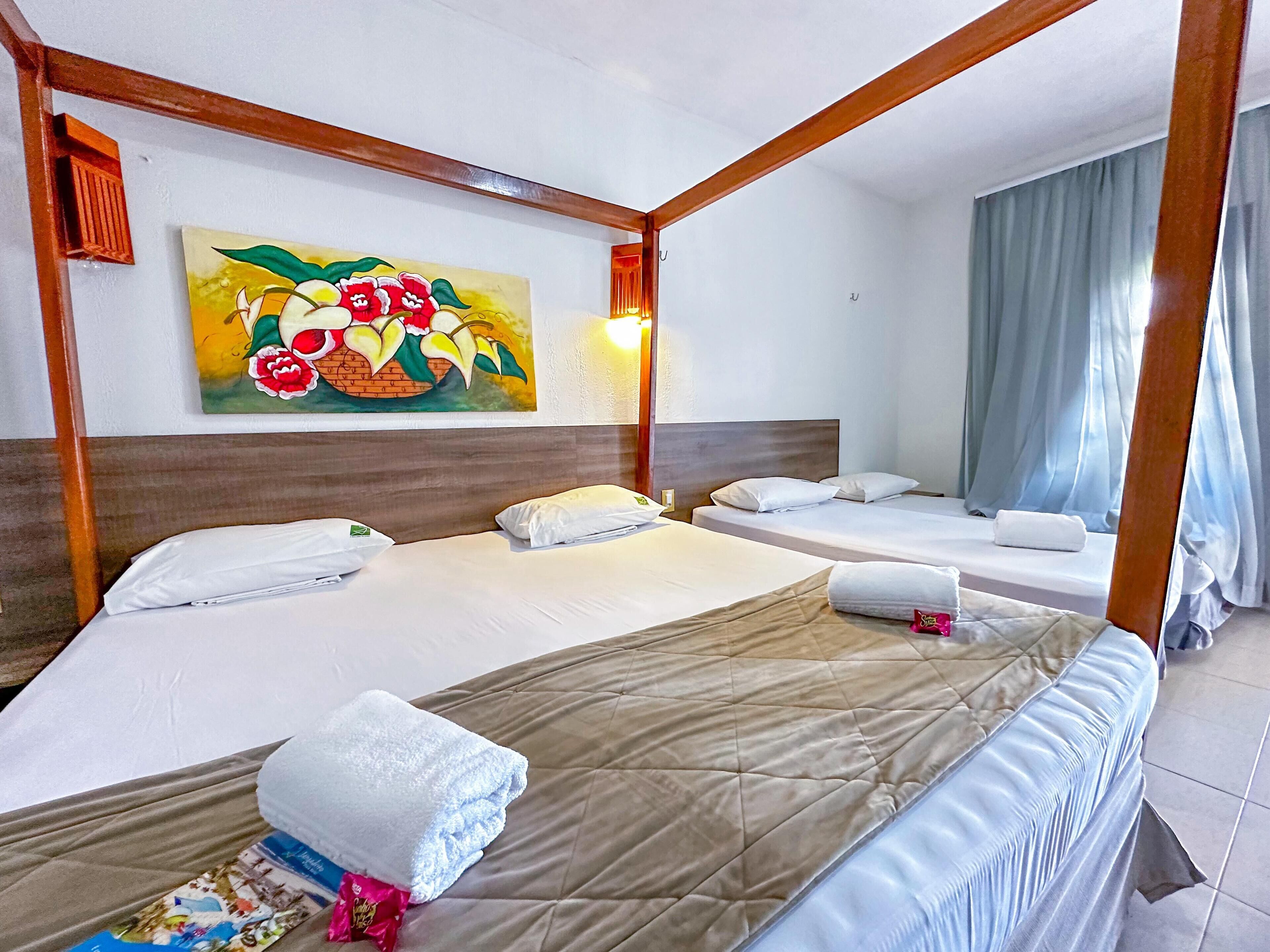 A hotel room with a four-poster bed, two single beds, a painting on the wall, and a window with curtains.